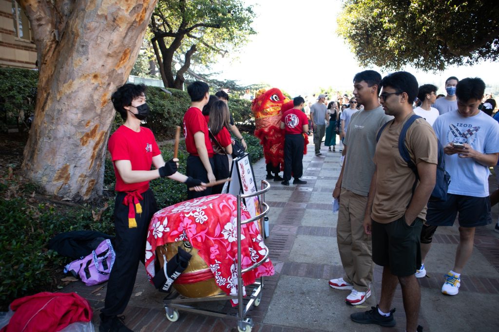 Samuel Lu, a member of the UCLA ACA Lion Dance Club, plays the drum for the students maneuvering the lion to dance to; to his right, Rohith Venkatesh, a computer science student, and Anand Kumar, a bioengineering student, watch him play. The Enormous Activities Fair draws in both new and returning students to join various organizations. Photo by Juan Cesar Perez/BruinLife.