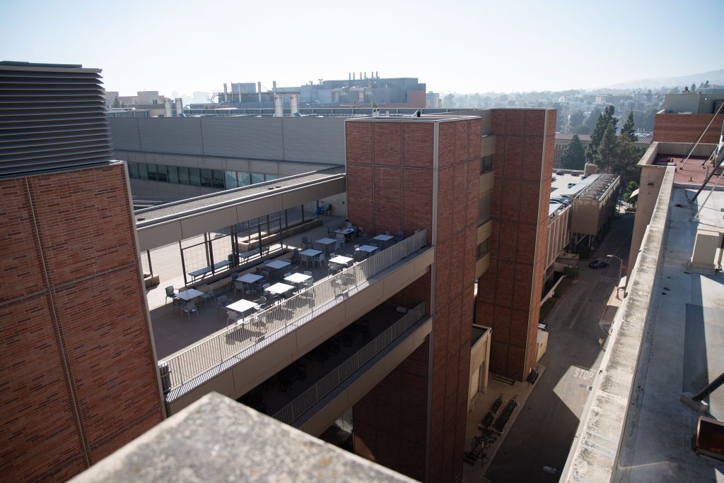 The southwest side of the roof of Boelter Hall opens up to the California NanoSystems Institute, as well as Parking Structure 9 and Engineering IV to the right. The distant hills appear to emerge from the horizon on a hazy day. Photographed by Julia Gu/BruinLife.