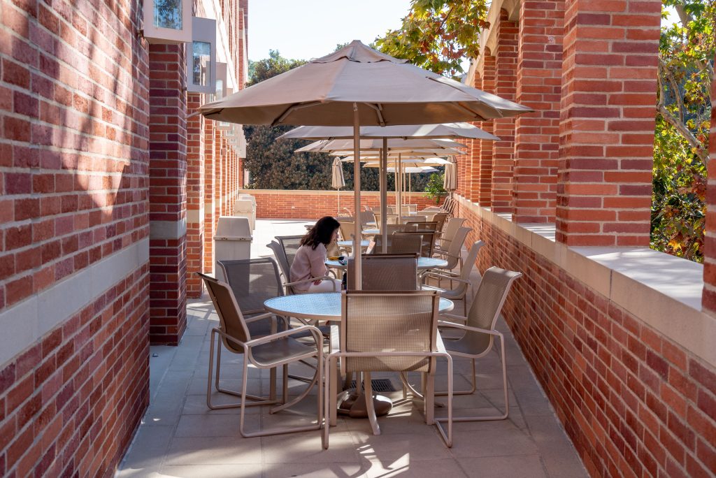 A student takes a call outside Gold Hall in the shade of bordering trees. Between events, the patio around the Executive Dining Room opens up to become a quiet study space of brick and greenery. Photographed by Julia Gu/BruinLife.