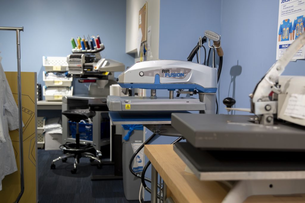 Alongside a printer, an embroidery station sits in the back of the Bruin Custom Print room, noticeably populated with extra blue and yellow thread. In addition to traditional paper printing services, Bruin Custom Print prints custom poster, banner, pin, sash and T-shirt designs.