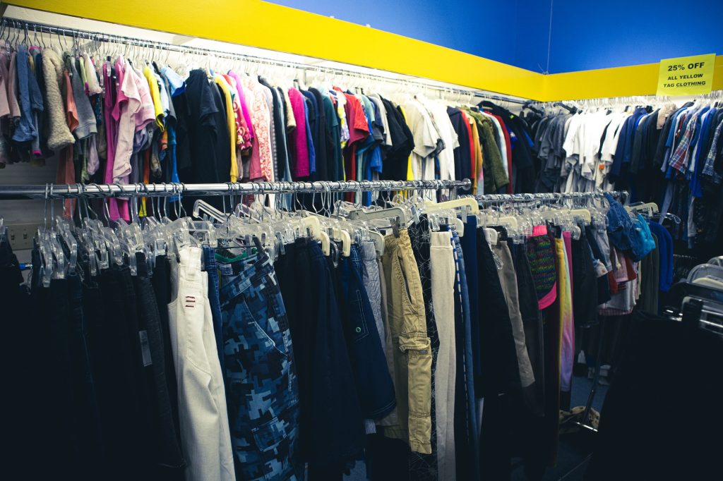 Racks of clothes tops hang above two racks holding clothes bottoms. The clothing racks are separated by garments and are well organized. This makes it enjoyable and easy to look for your desired garment to complete that outfit in your mind.