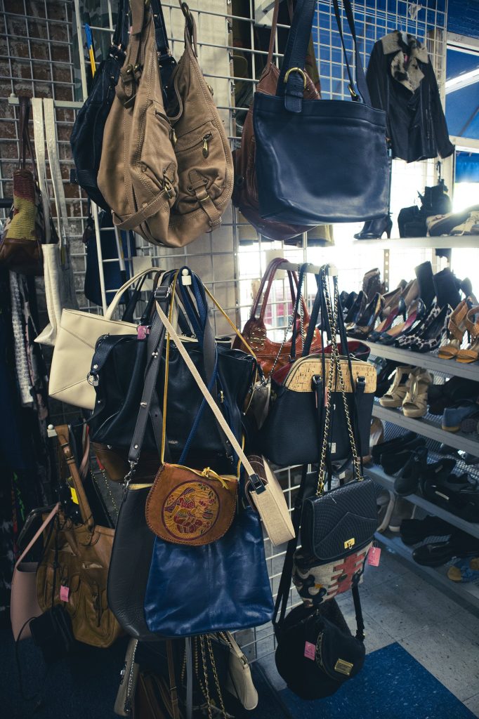 Various handbags hang on a wire wall rack. On top of clothes, you can find a huge variety of clothing accessories like purses, jewelry, handbags, watches and much more.