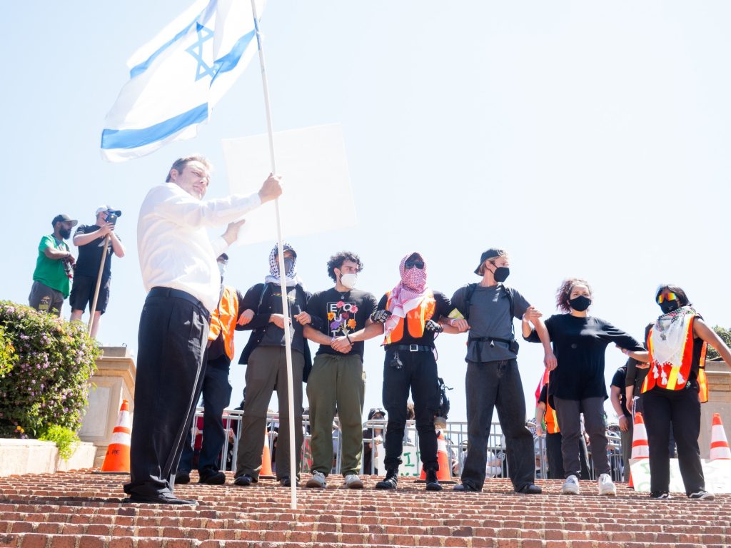 A pro-Israel protester carries the flag of Israel up to the perimeter of Janss/Kuruvungna Steps facing the side of the encampment. Photographed by Finn Martin/BruinLife.