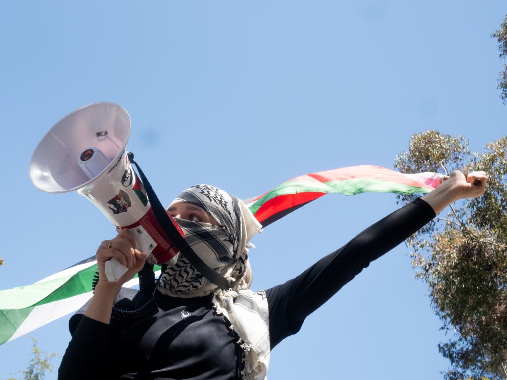 A pro-Palestine protester waves the flag of Palestine while speaking through a megaphone. Photographed by Finn Martin/BruinLife.