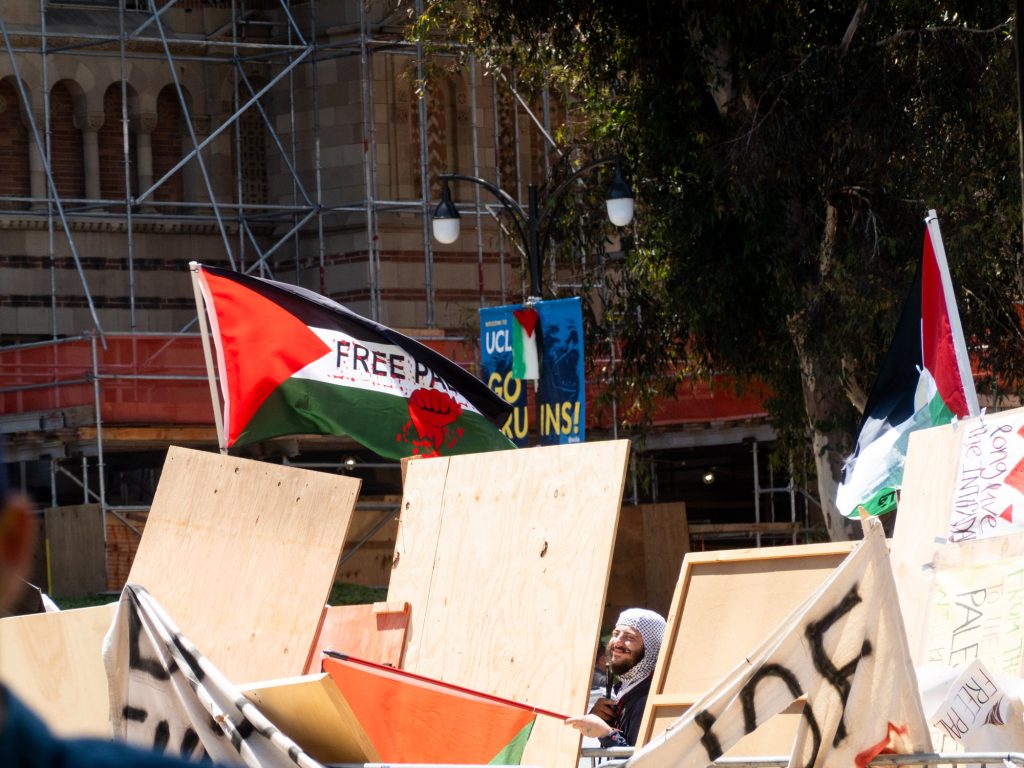 A pro-Palestine protester lowers their mask to smile at the pro-Israel side. Per the Daily Bruin, security forces were engaged by UCLA to maintain a no-access zone between the two protest groups. Photographed by Finn Martin/BruinLife.