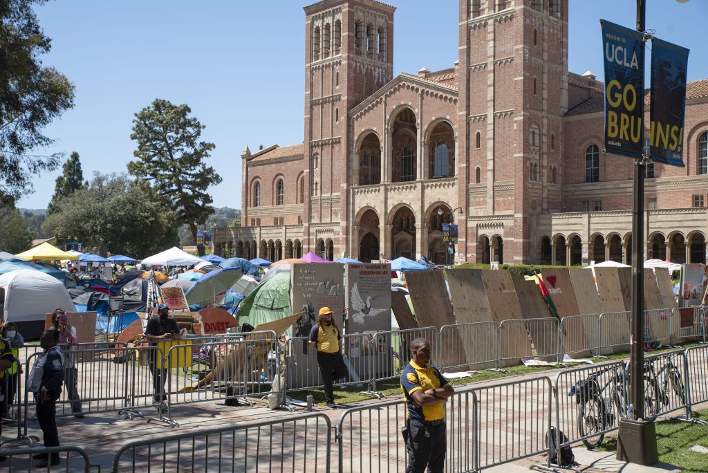 The pro-Palestine encampment envelops the grass in front of Royce Hall. Metal fences and wooden boards create a barrier denying access to the encampment. Photographed by Emily Chandler/BruinLife.