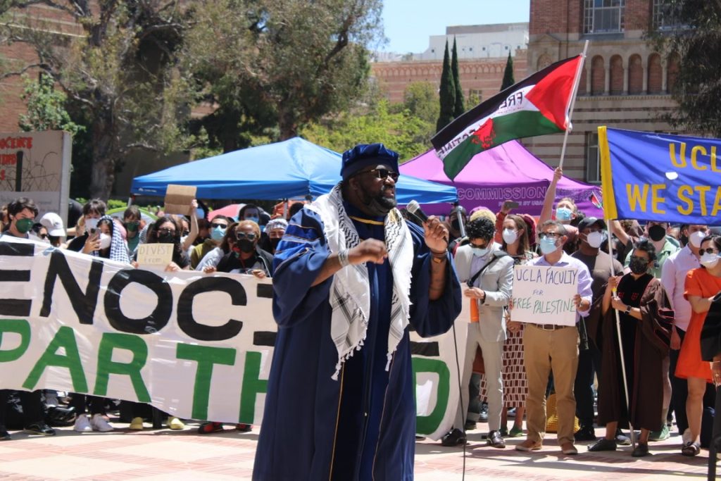 A pro-Palestine speaker addresses the crowd inside the encampment. Faculty members affiliated with the UCLA Faculty pro-Palestine movement can be seen standing in solidarity.  Photograph provided by the Encampment Document Team.