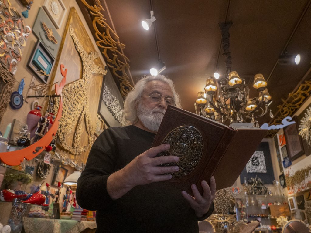 Bahman Bennett, the founder of Gallery Eshgh, reads through an ornately decorated book of Persian poetry. His gallery is a trove for Persian art and artifacts, all arranged around themes of love and inclusion.