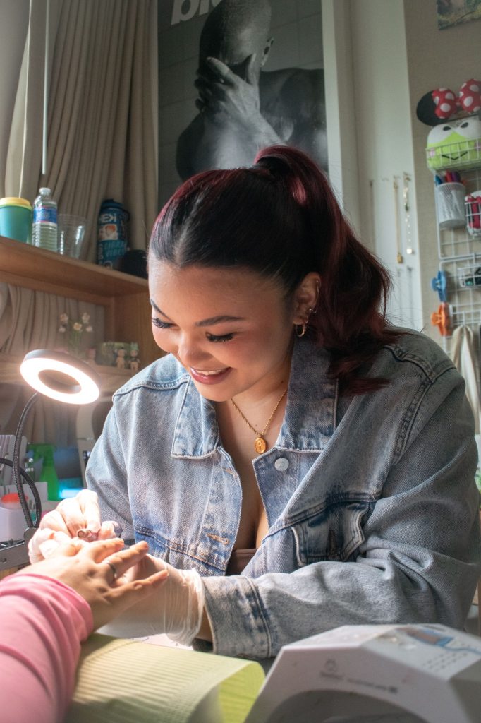 Mia Pryzbus smiles as she works on a client's nail set. Pryzbus has created a workspace in her dorm room.
Photographed by Emily Chandler/BruinLife