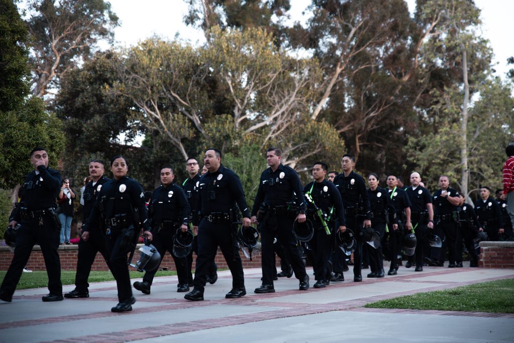 Police officers walk through Dickson Court North with face protection and crowd control weapons. Police forces shuttled across campus to prepare to enter the encampment. Photographed by Caleb Velasquez/BruinLife.