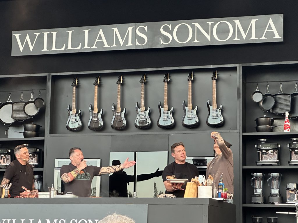 Tyler Florence, Liam Mayclem, a helping chef and Tommy Lee eat slices of meat at the Williams Sonoma Culinary Stage.