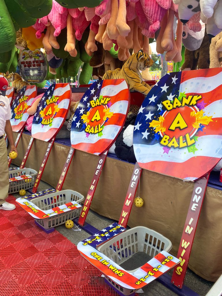 Several "Bank a Ball" game baskets lean against the wall of a game tent. The carnival game had the simple rules of just banking a ball into a bucket to win, with the baskets holding signs that said "one in wins."