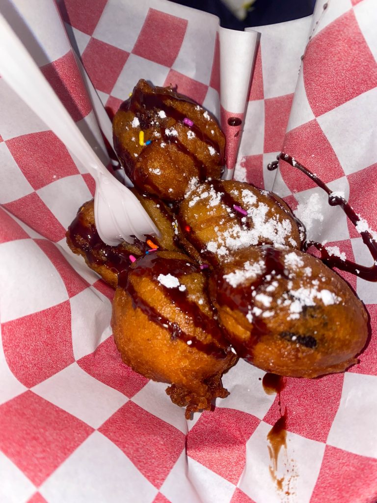 Fresh deep-fried oreos covered with chocolate syrup, powdered sugar and sprinkles.