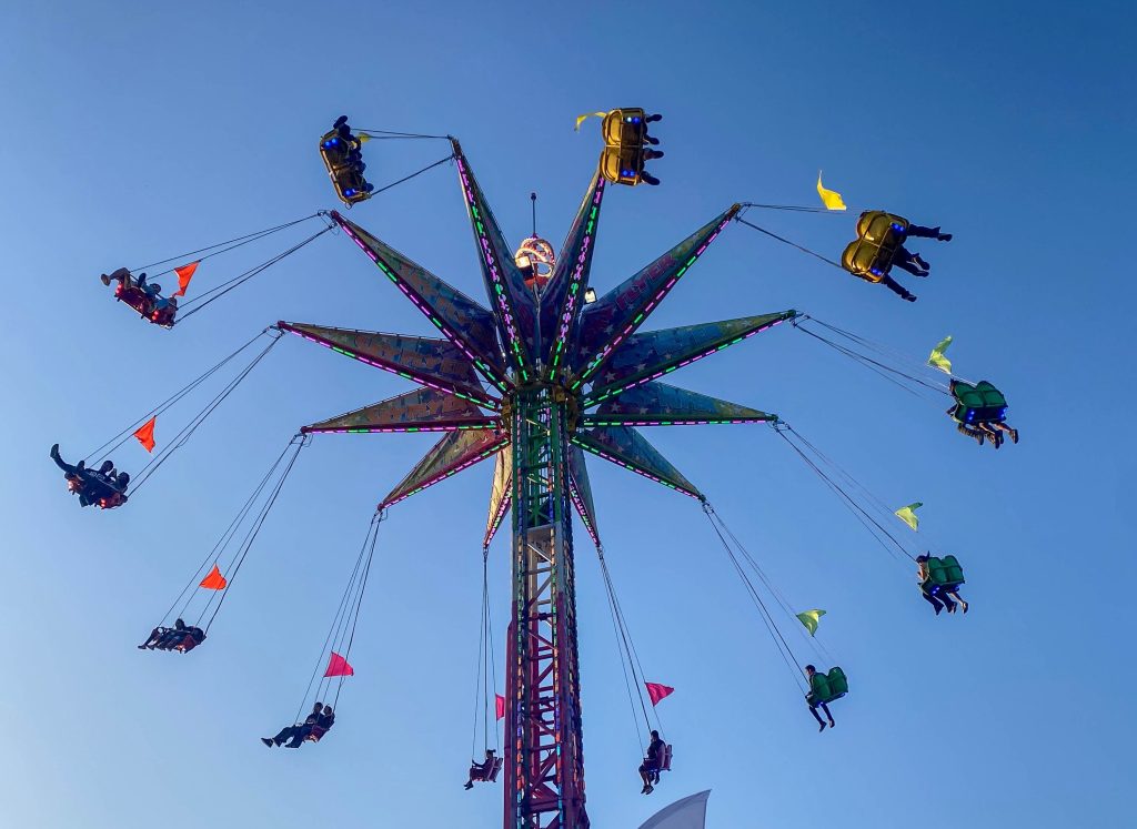 On one of the fair rides, people sit suspended up in the air on swings that rotate high up above the rest of the fair.