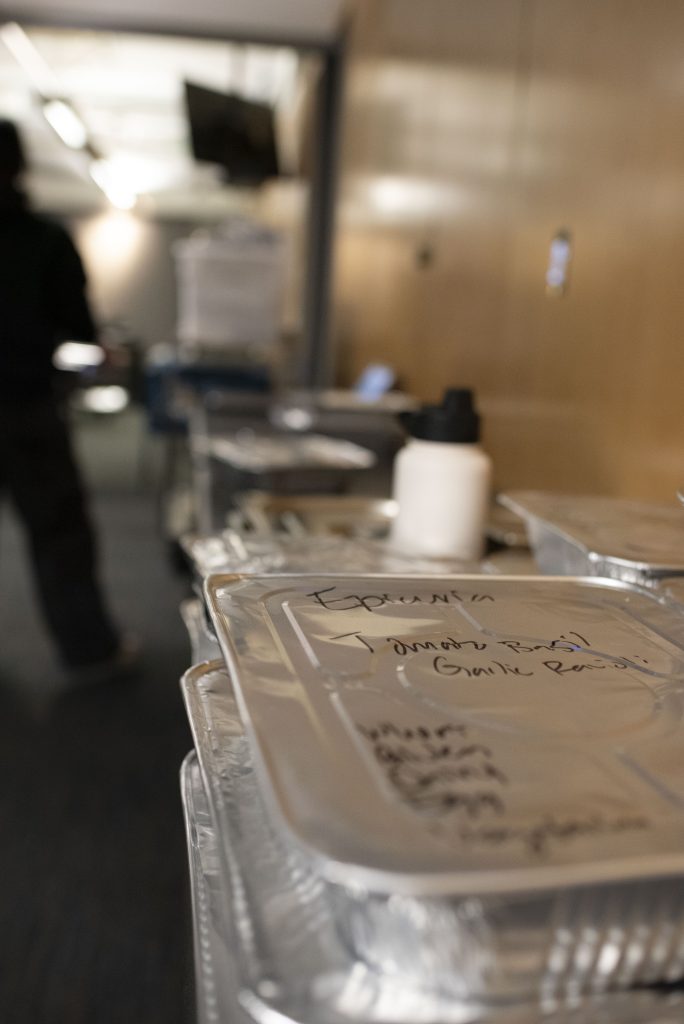 In the minutes leading up to 10 PM, a carefully-labeled tray from Epicuria prepares to be served. Bruin Dine volunteers also prepare, using the period between food recovery and food distribution to wash their hands and tie hair back. Photographed by Julia Gu/BruinLife