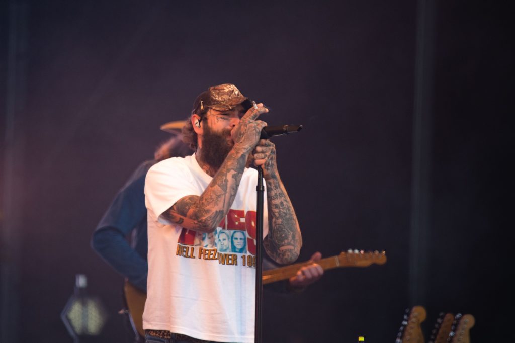 After a roar of applause, Post Malone begins to sing, grabbing the microphone with both hands as a cigarette is also held in one of them. Photographed by Caleb Velasquez/BruinLife.