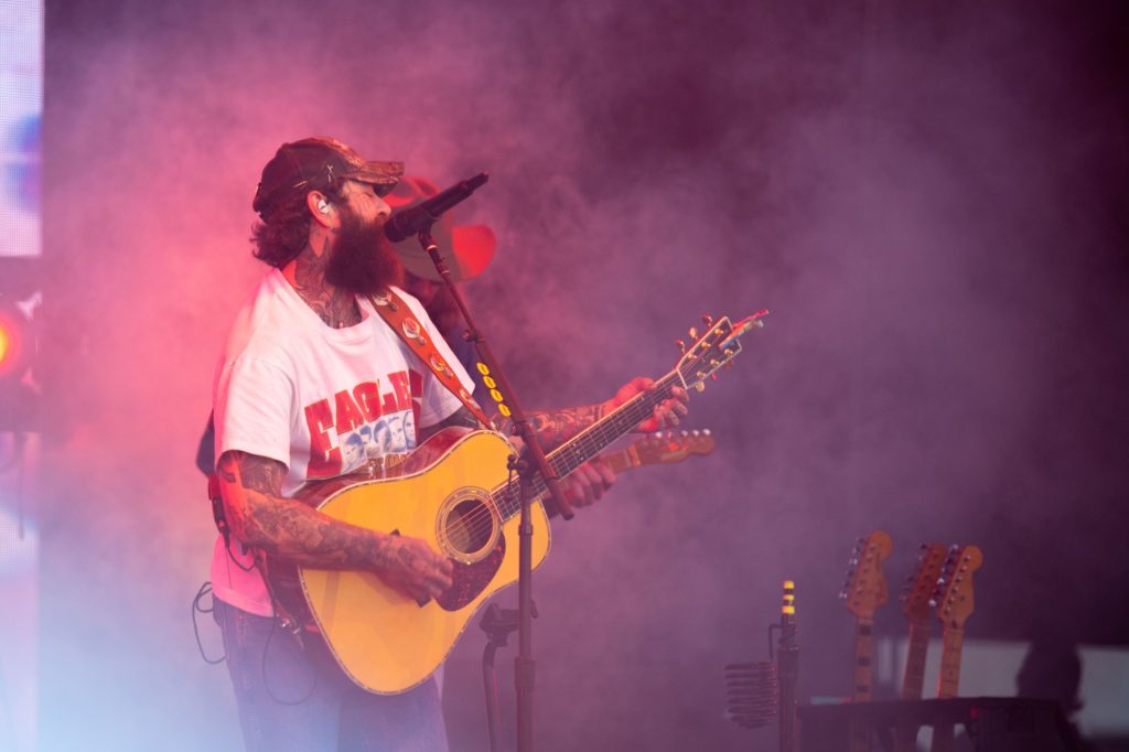 Post Malone picked up his guitar to perform a rendition of "Carrying Your Love with Me," by George Strait. Smoke and haze shrouded the artist as this time fire shot up into the sky. Photographed by Caleb Velasquez/BruinLife.