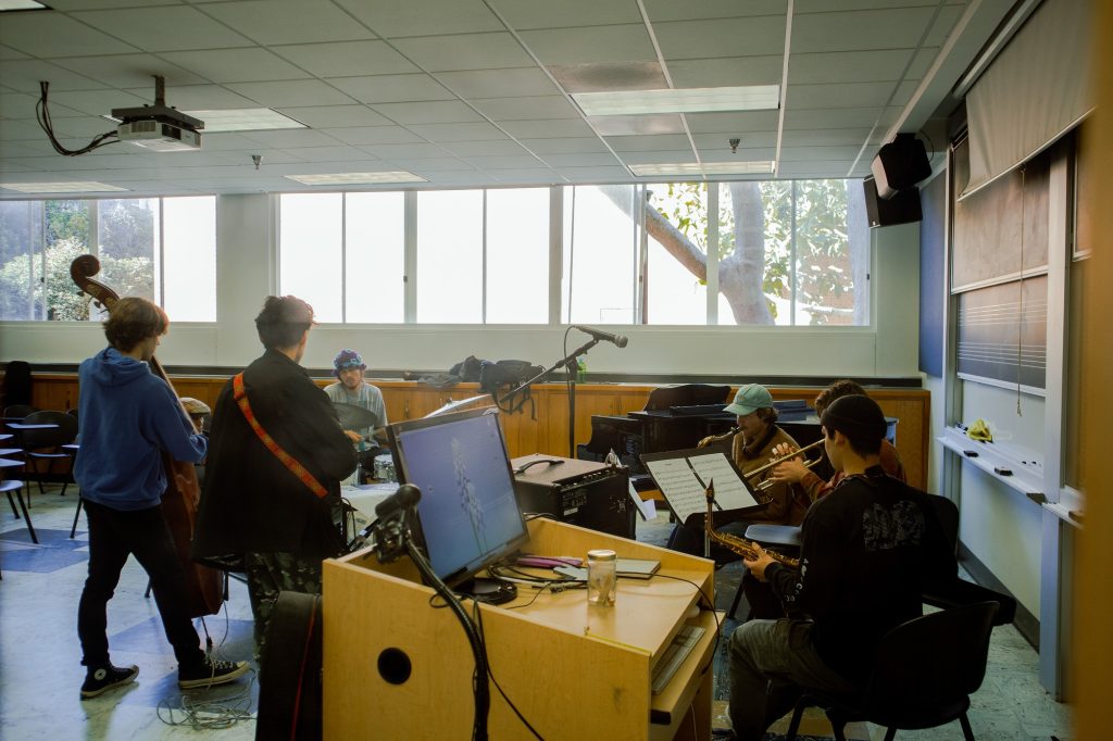 UCLA students rehearse together in a classroom, playing a variety of instruments as part of a music ensemble. The relaxed atmosphere and teamwork showcase the vibrant creative community on campus.