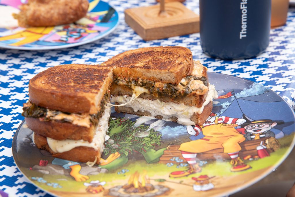 Collard Green Melt served with crinkle-cut fries. The sandwich features toasted bread, spicy mayo, sweet chili-coated collards, creamy cabbage slaw, and rich cheese, combining bold flavors and textures.