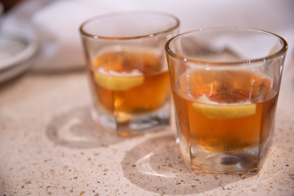 Two tumblers filled with New Orleans sazeracs, a whiskey rye with bitters and a lemon slice.  Photographed by Finn Martin/BruinLife.