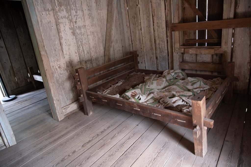 A reconstruction of a barely sheeted bed frame inside a cabin where the enslaved lived. Photographed by Finn Martin/BruinLife.