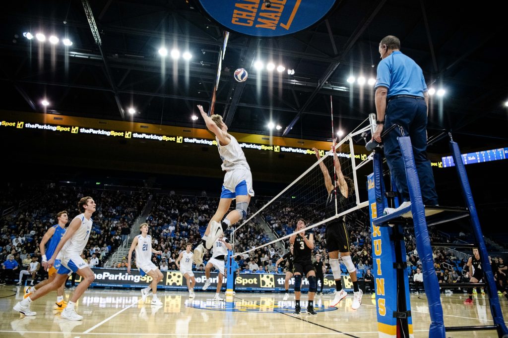 UCLA's Cooper Robinson leaps high to spike the ball over Long Beach State defenders. Photographed by Ryan Zhang/BruinLife.