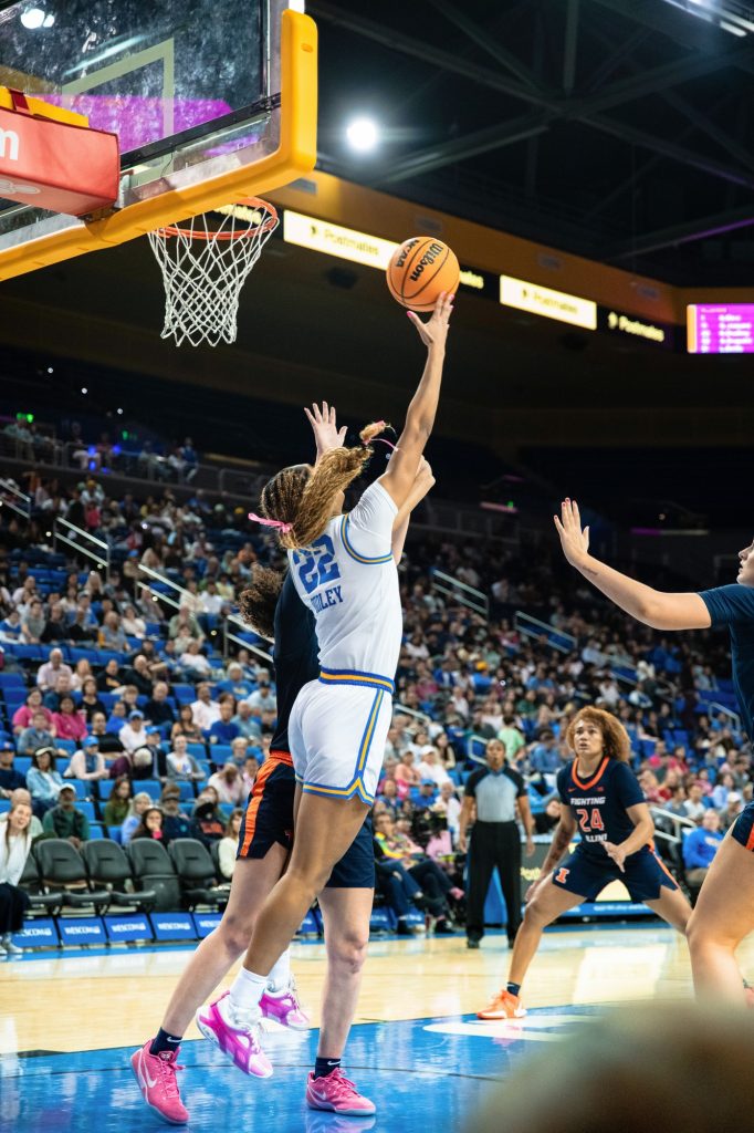 UCLA #22 Kendall Dudley drives under the basket and scores a reverse layup over Illinois defense. Photographed by Ryan Zhang/BruinLife