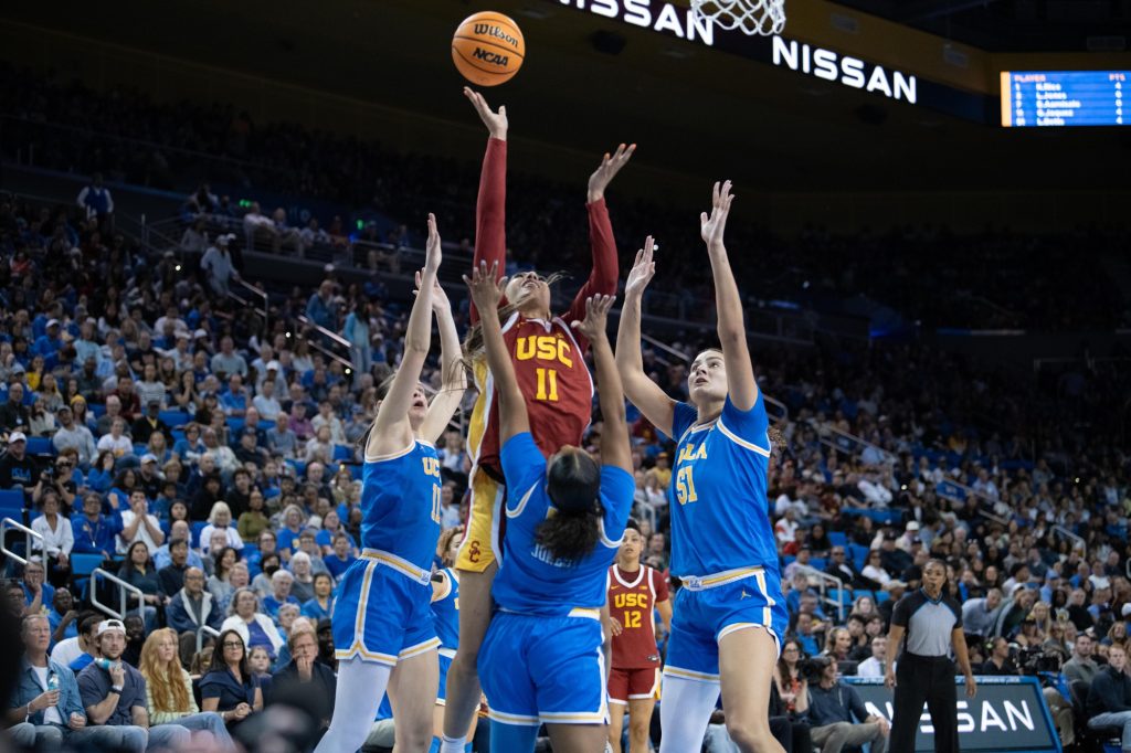 Three UCLA players jump in the air to defend against USC's Kennedy Smith as she takes a shot.