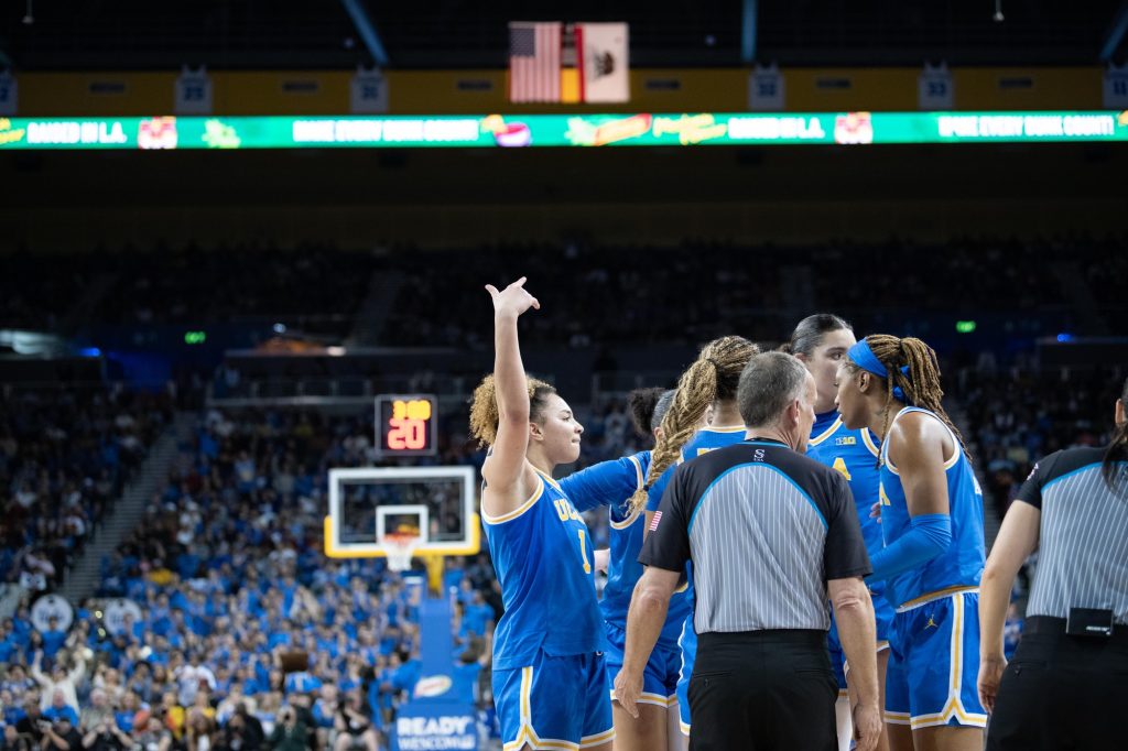 Point guard Kiki Rice summons cheers from crowds with hand motions in the air after a jump ball call with an opposing player.