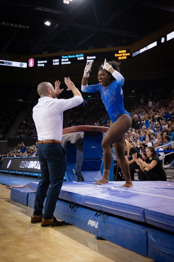 Senior Chae Campbell celebrates with her coach after she sticks the landing on her vault routine. Photographed by Cathryn Kuczynski/BruinLife.