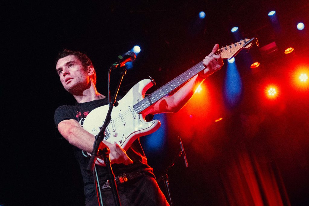 Lead vocalist and guitarist Kai James of Girl and Girl lifts his guitar mid-song while looking over the crowd. Photographed by Amy Miranda/BruinLife.