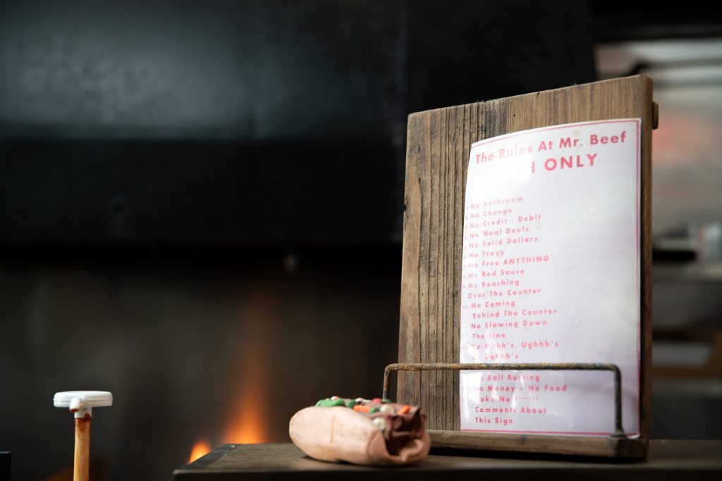 The house rules for Mr. Beef sit atop the counter, alongside a mock-up of one of their delicious sandwiches. Photographed by Finn Martin/BruinLife.