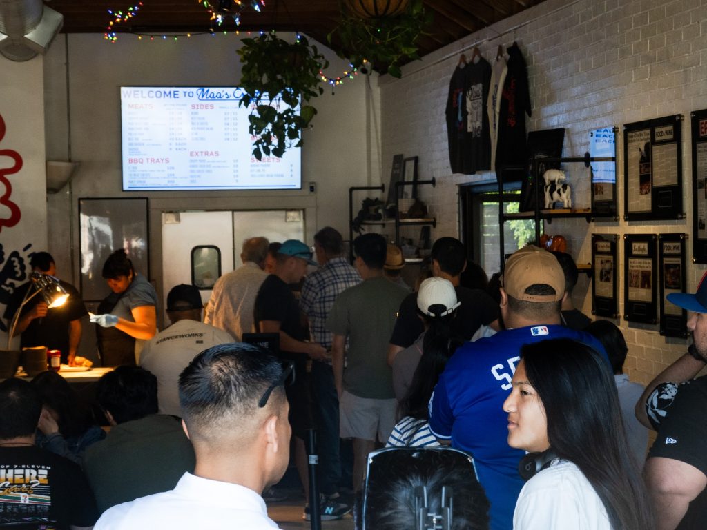 The line queues customers against eye-raising signage by some of the food scene's finest outlets giving praise for Moo's Texas-style barbecue. On occasion, a voice on the microphone took attention away from the wall-written reviews to reassure patrons not to abandon the line. Photographed by Finn Martin/BruinLife.